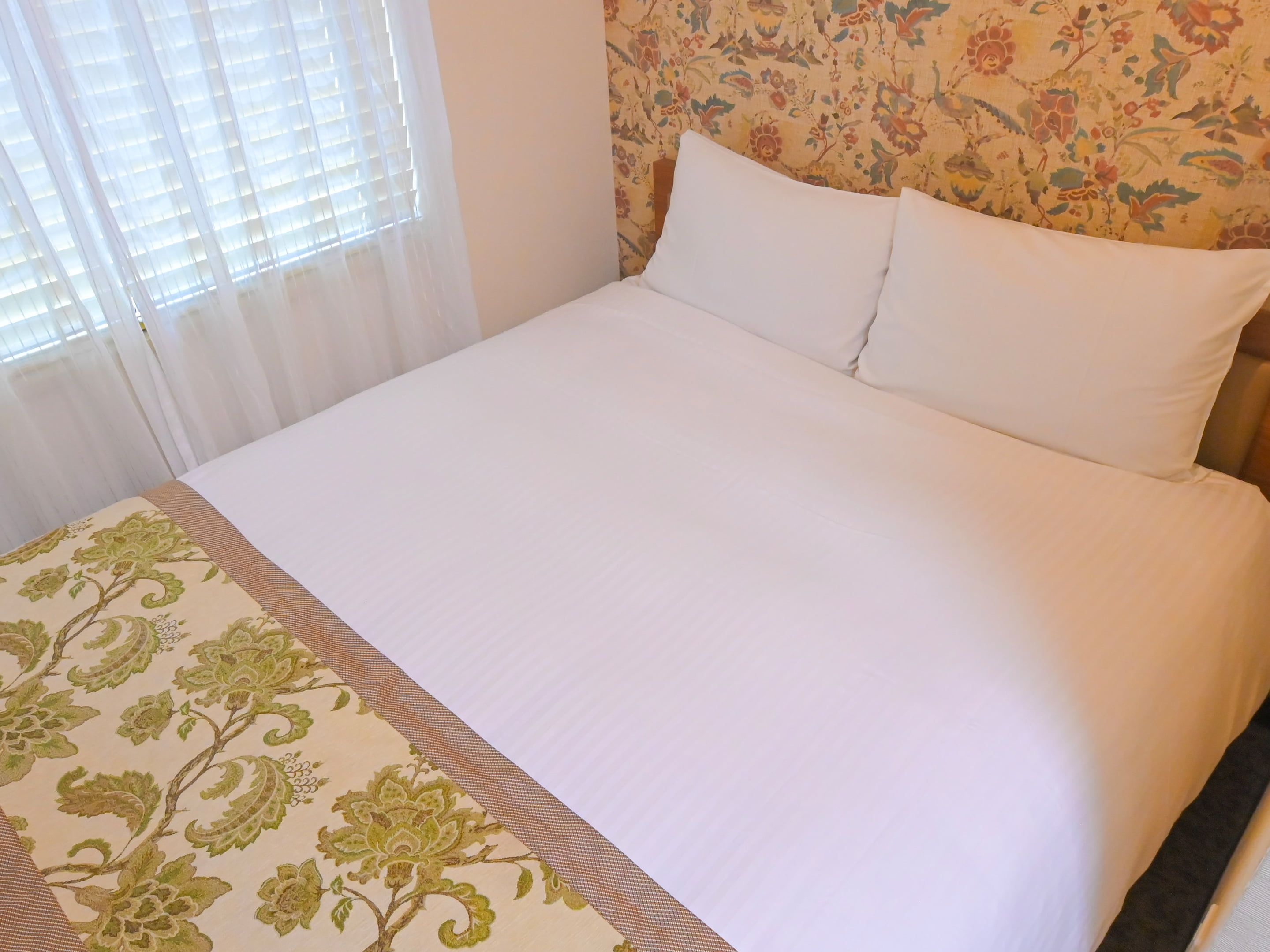 Una cama con sábanas blancas y una colcha estampada con motivos florales.