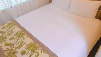 Una cama con sábanas blancas y una colcha estampada con motivos florales.