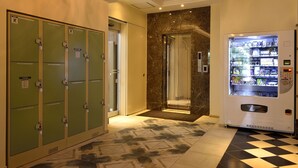 Un vestíbulo de hotel con taquillas verdes, una pared de mármol, un ascensor de vidrio y una máquina expendedora.