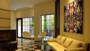 Una sala moderna con suelo a cuadros, un sofá, dos sillones blancos, una mesa de centro de vidrio, un televisor de pantalla plana y un cuadro abstracto de gran tamaño en la pared.