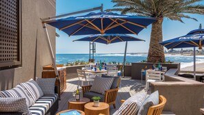 Une terrasse en bord de mer avec des espaces pour s’asseoir à l’extérieur, des parasols et une vue sur l’océan.