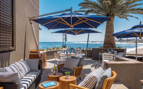 A seaside patio with outdoor seating, umbrellas, and a view of the ocean.