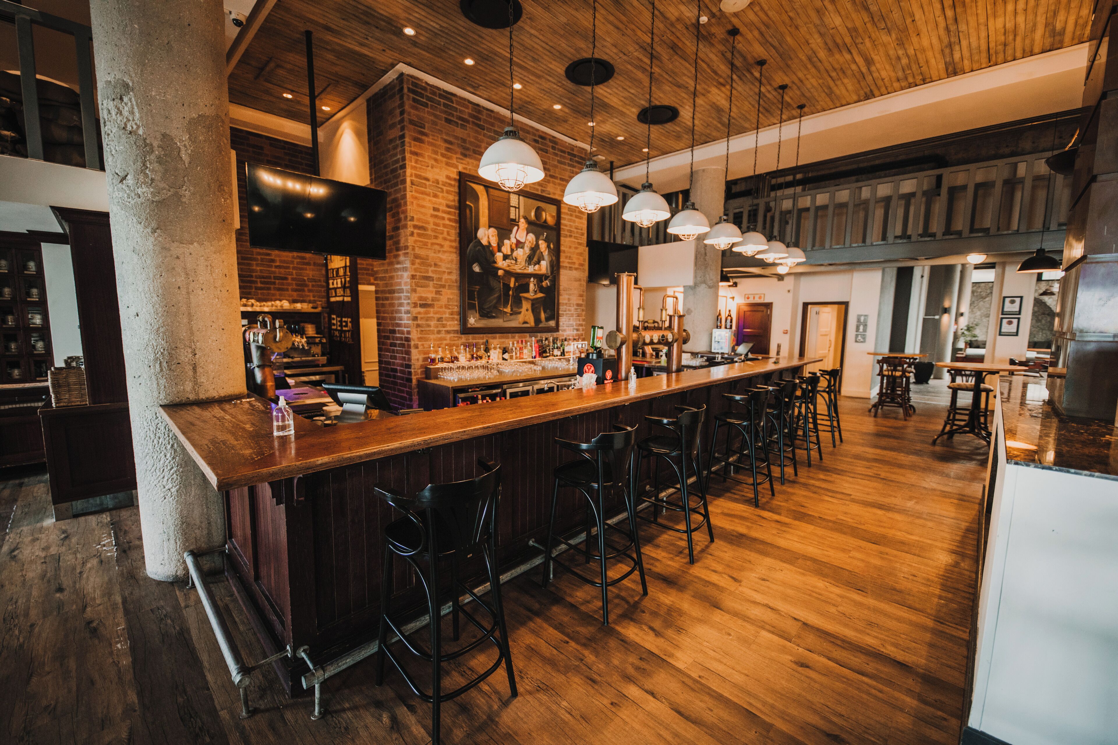 Un área de bar con suelo de madera, taburetes y lámparas colgantes.