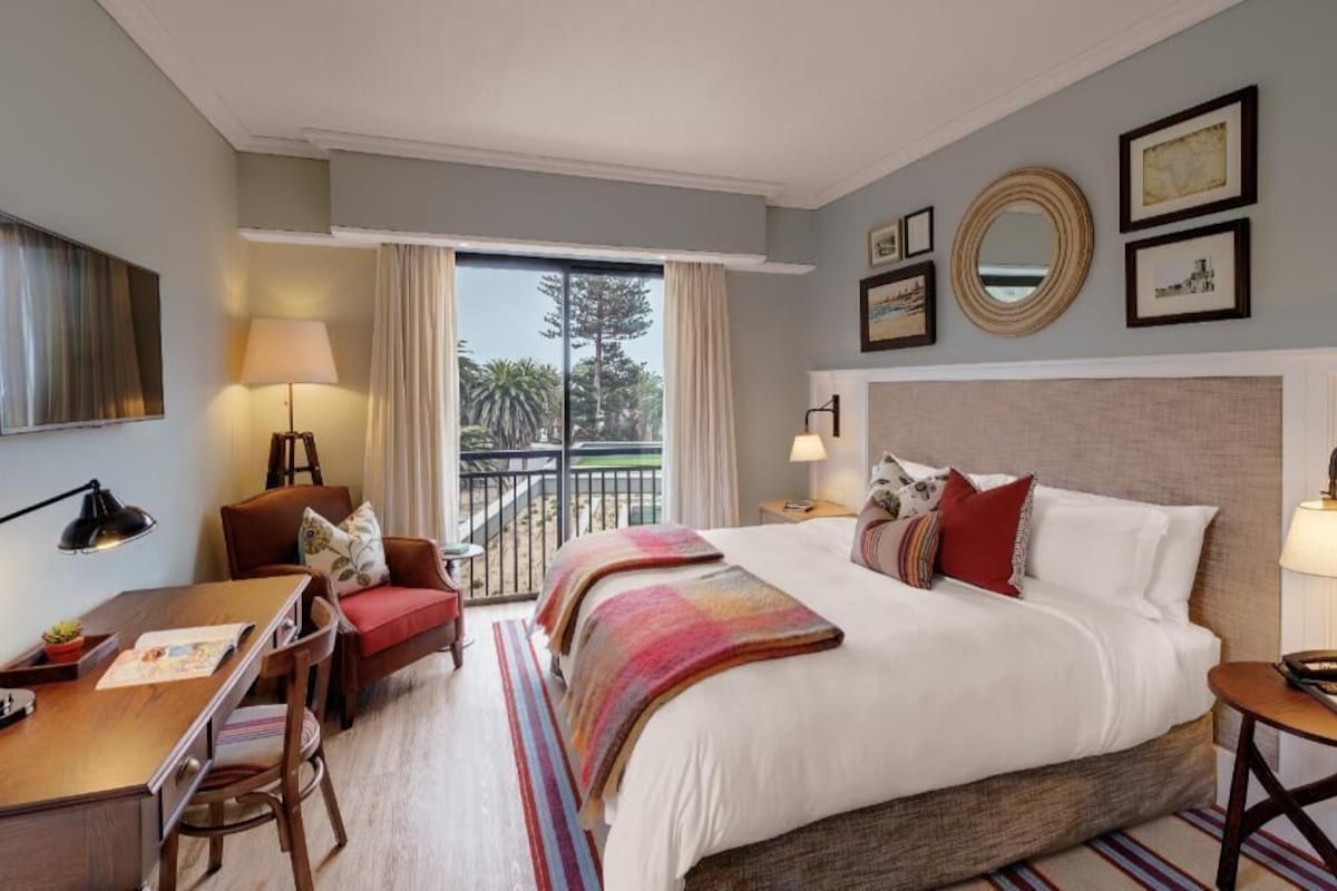 Habitación de hotel con cama, escritorio, silla y balcón con vistas.