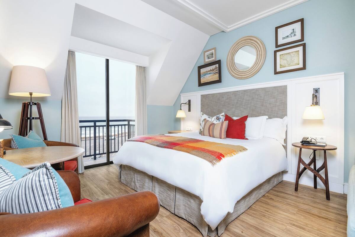 Ein Hotelzimmer mit einem großen Bett, einem Balkon, einem Essbereich und einem kleinen Tisch.