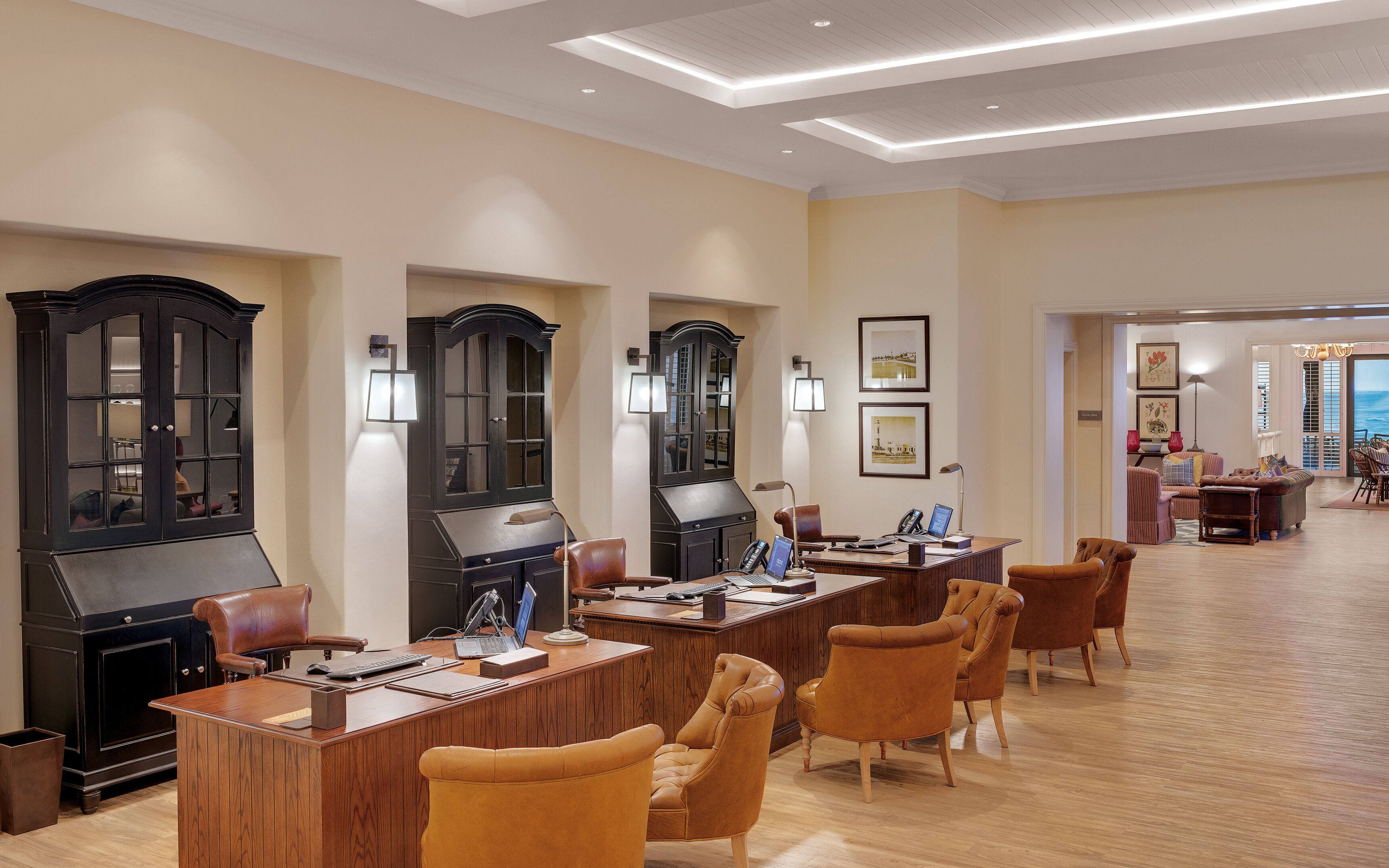 Un amplio hall de hotel con varias mesas de madera, sillas de cuero y un gran mueble de madera oscura.