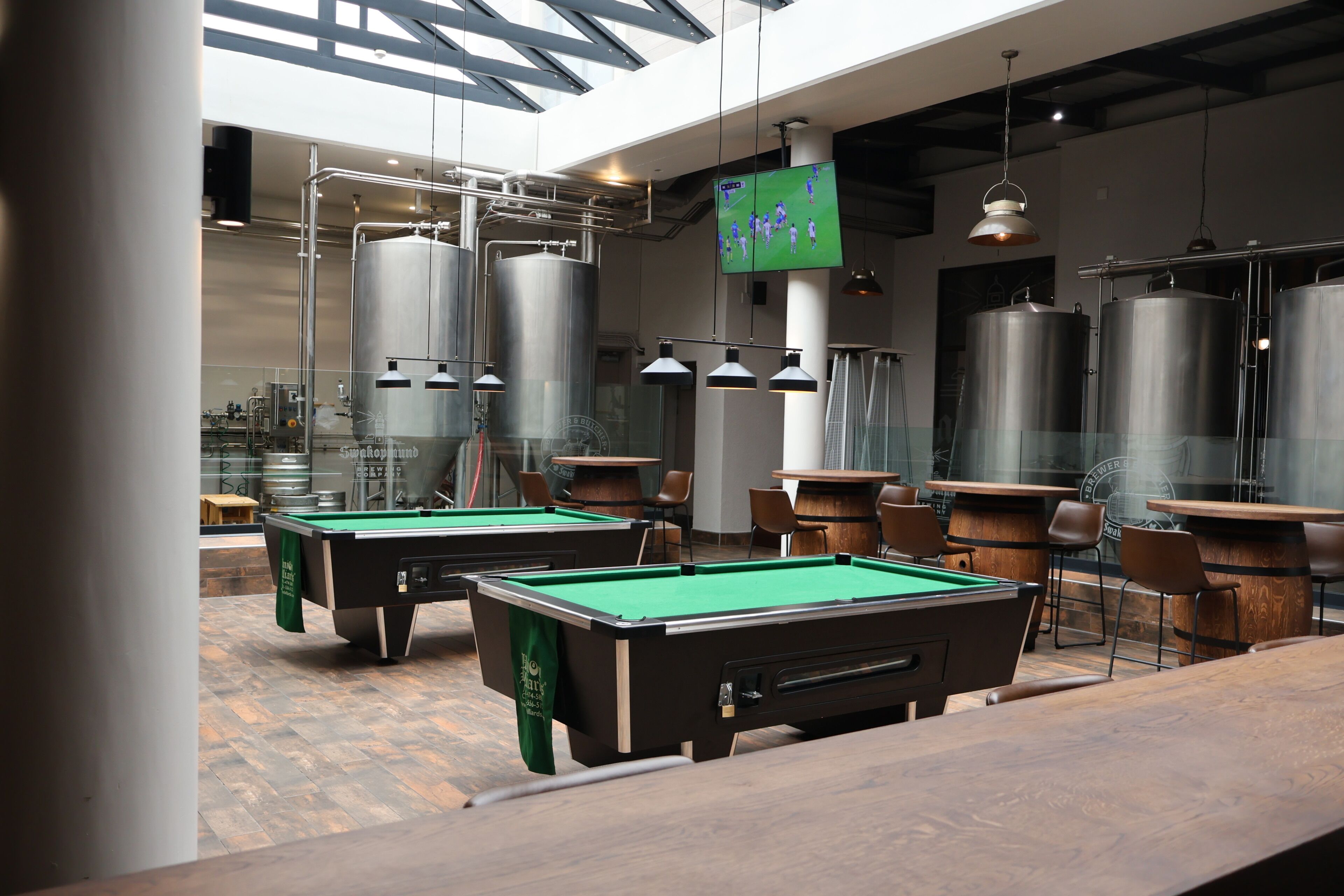 Een biljartkamer met tafels, stoelen en industriële tanks.