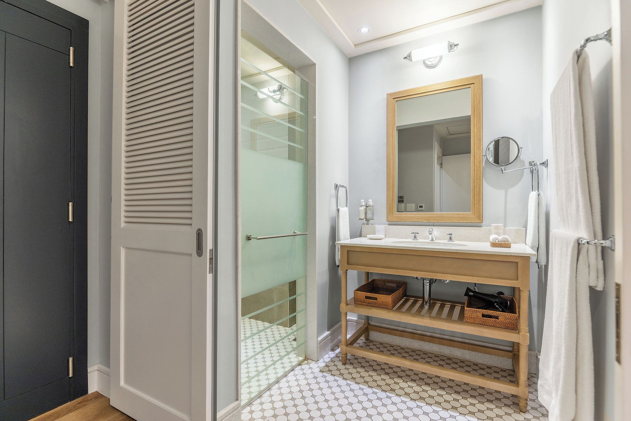 Un baño con ducha envuelta en vidrio, tocador de madera y un espejo grande.