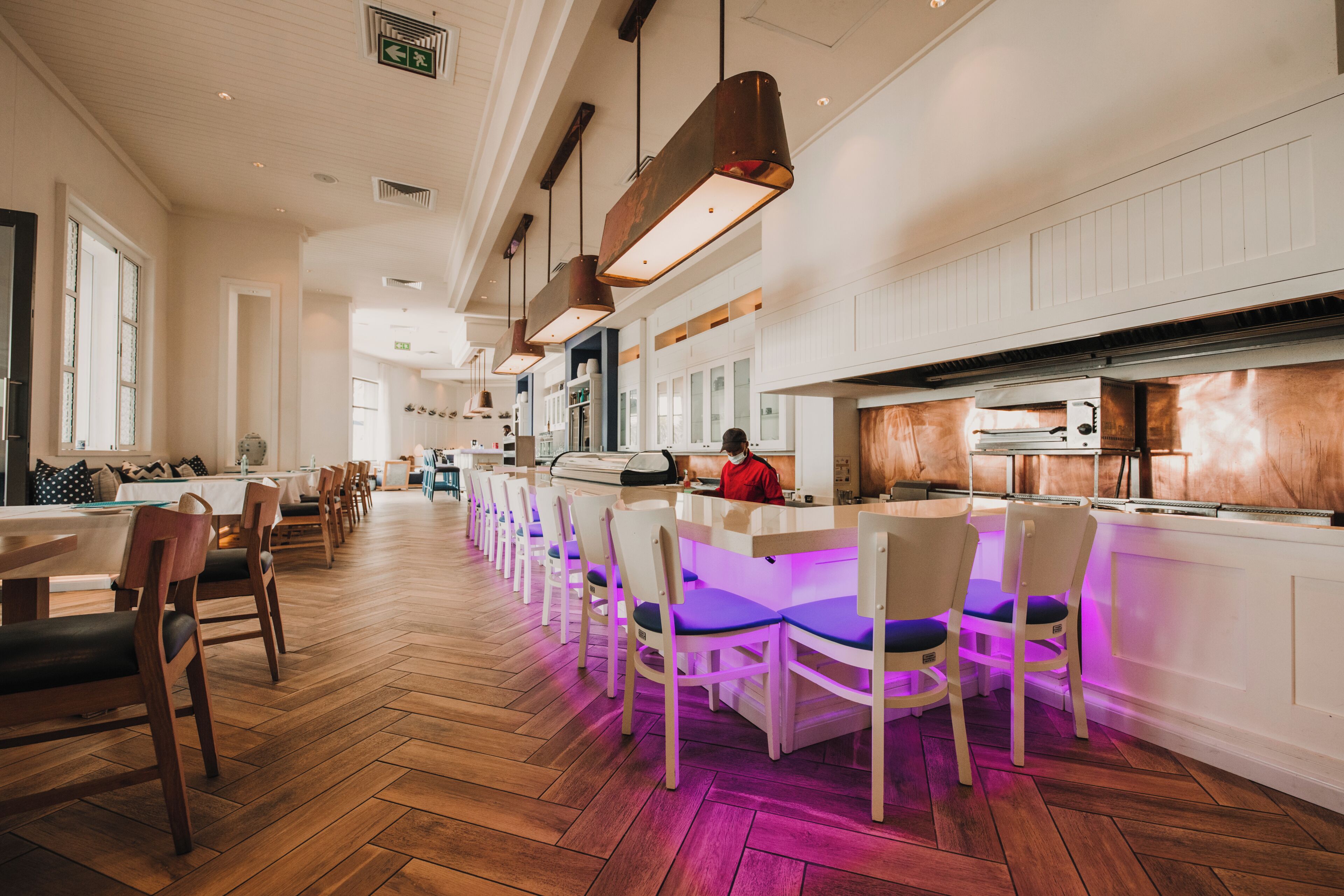 Un amplio vestíbulo de hotel con una larga recepción, varias zonas de estar y una cocina.
