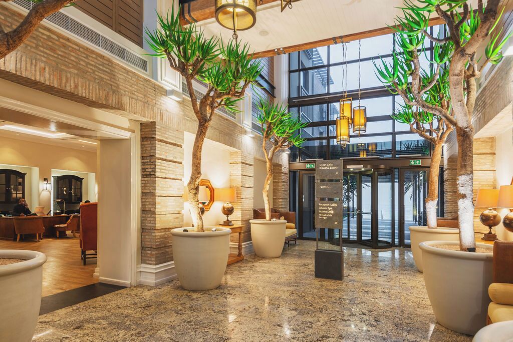 A lobby with a reception desk, potted plants, a glass door entrance, and a view of the outside.