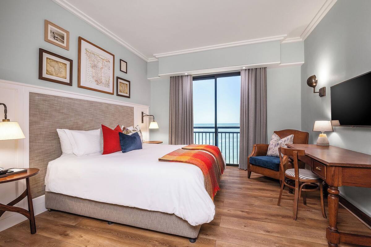 Ein Hotelzimmer mit einem großen Bett, einem Schreibtisch, einem Sessel und einem Fernseher. Vorhänge und ein Fenster mit Blick sind vorhanden.