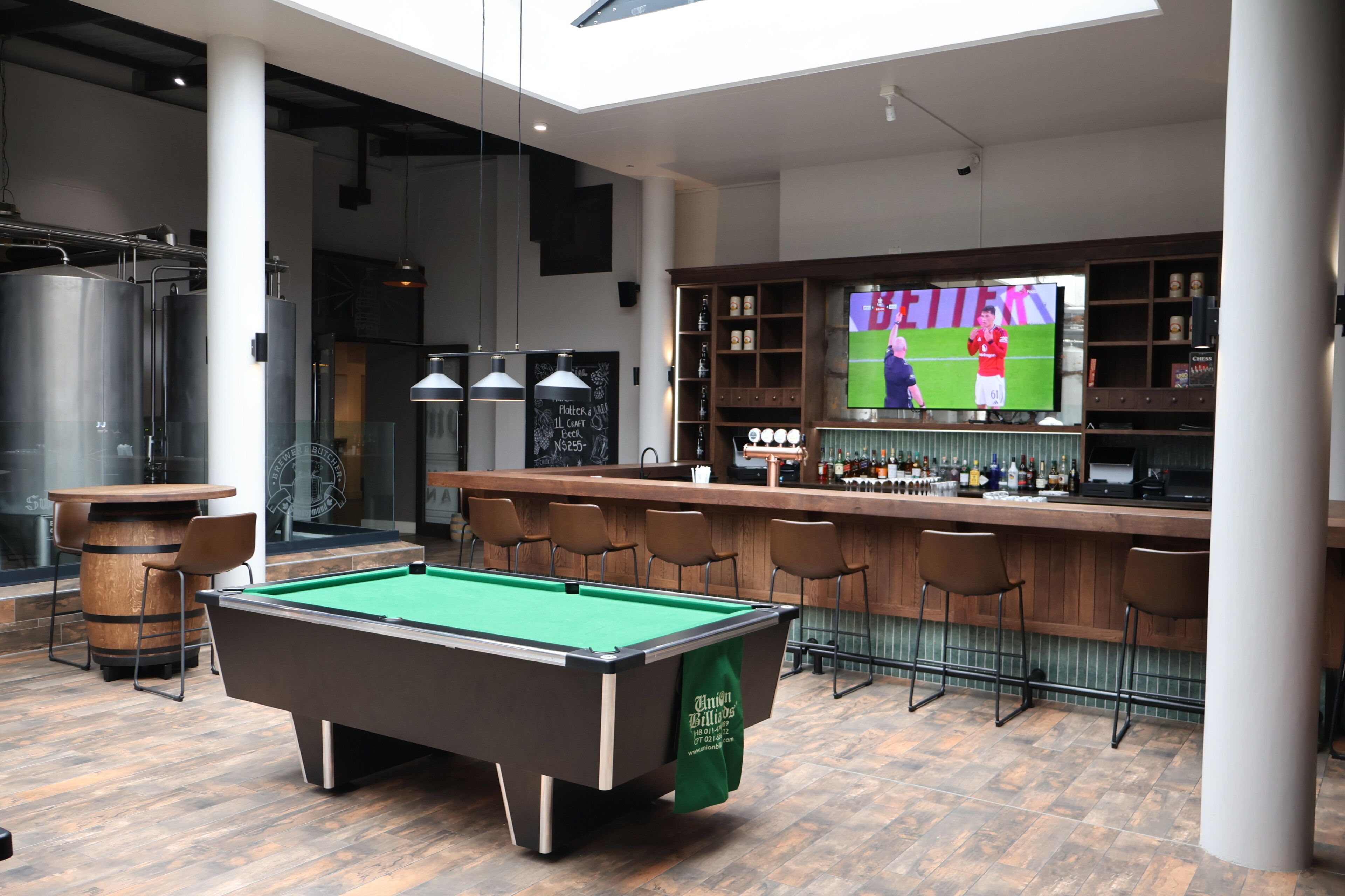 A pool table, bar area, and a television displaying a sports event in a modern indoor setting.