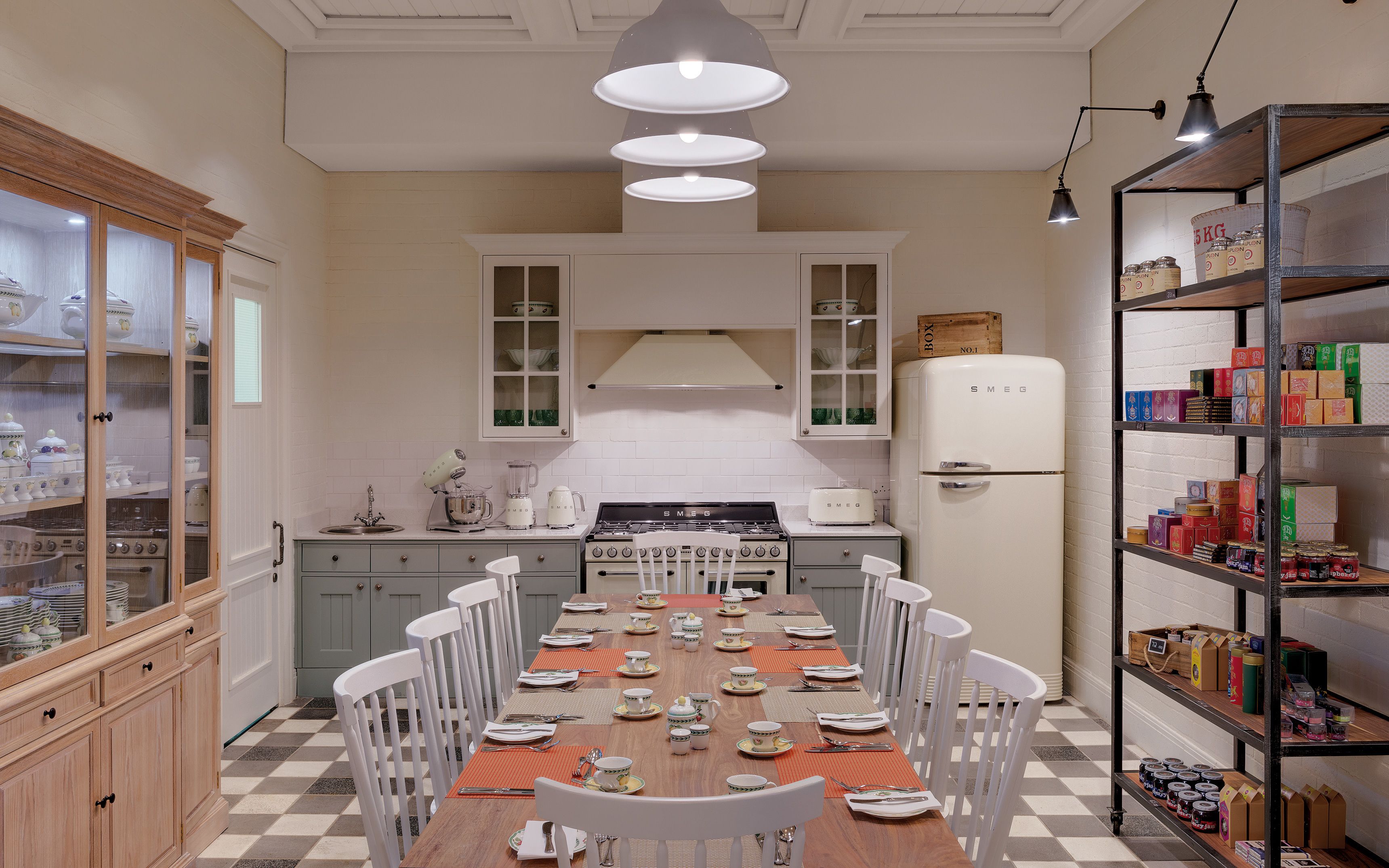 A kitchen with a dining table set for four, a stove, a refrigerator, and shelves with food items.