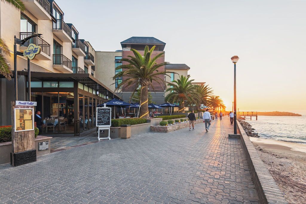 Paseo marítimo con un café, palmeras y un atardecer.
