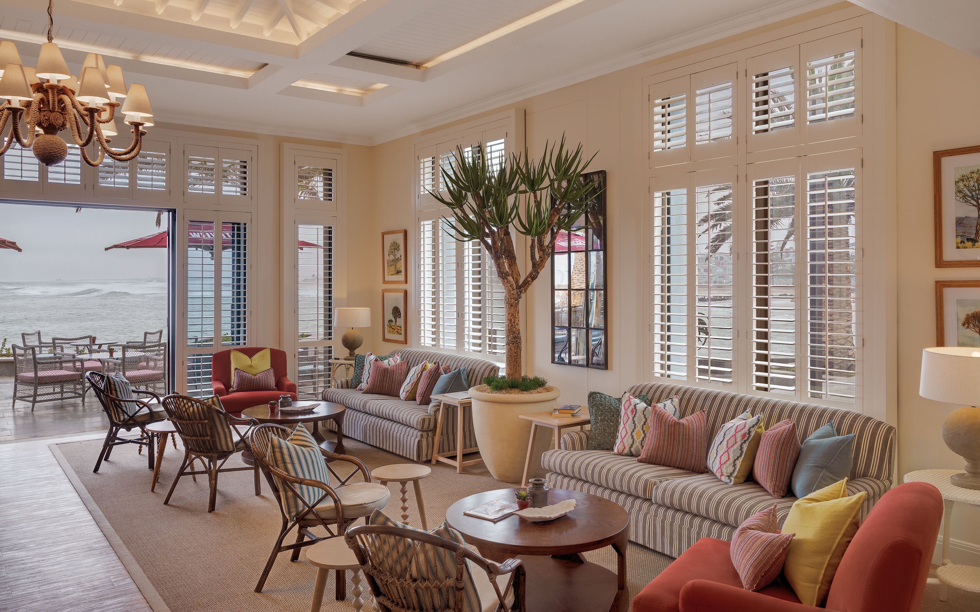 A spacious living room with a large window overlooking the ocean, furnished with a sofa, chairs, and a coffee table.