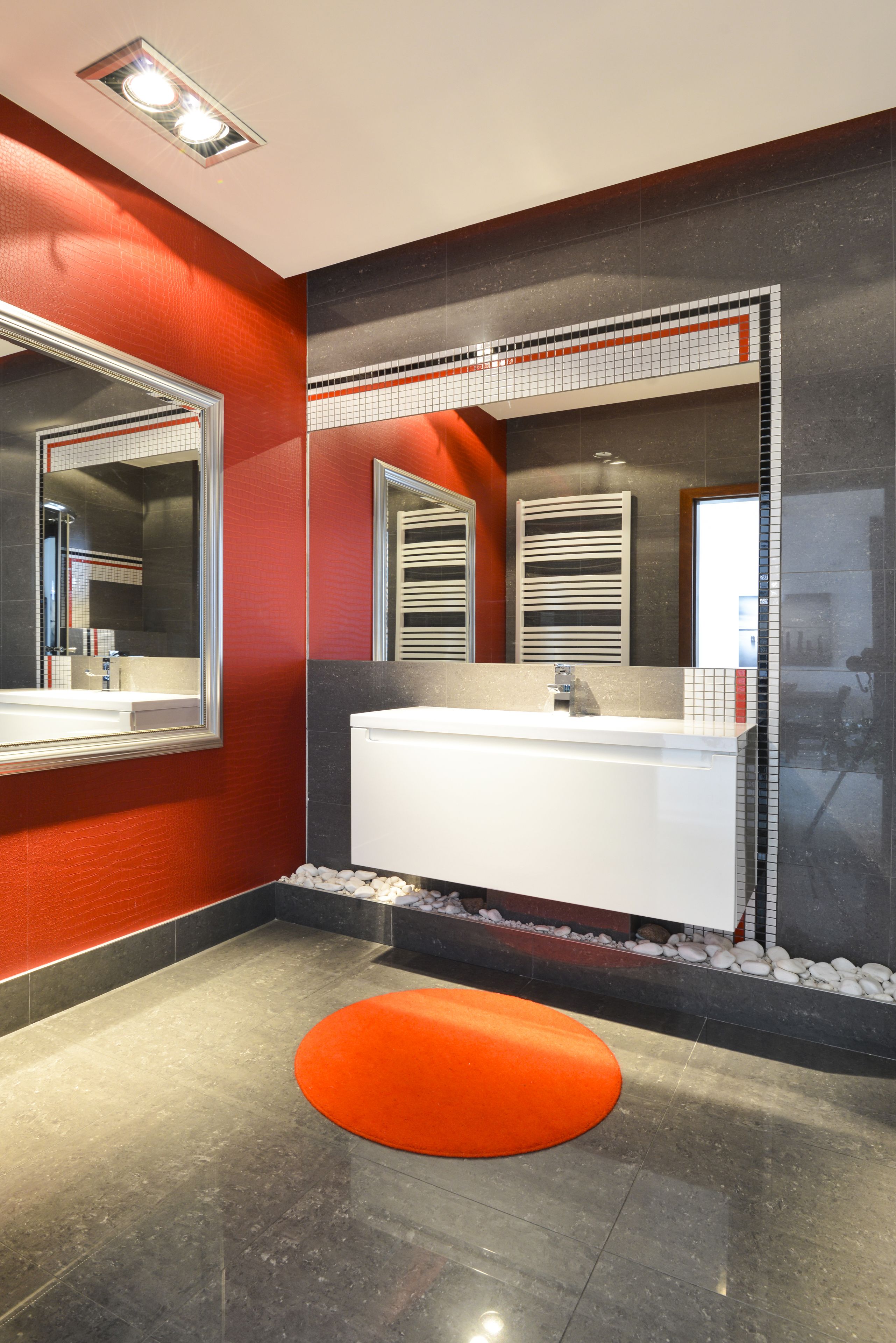 A modern bathroom with a white vanity, a large mirror, and a red accent wall.