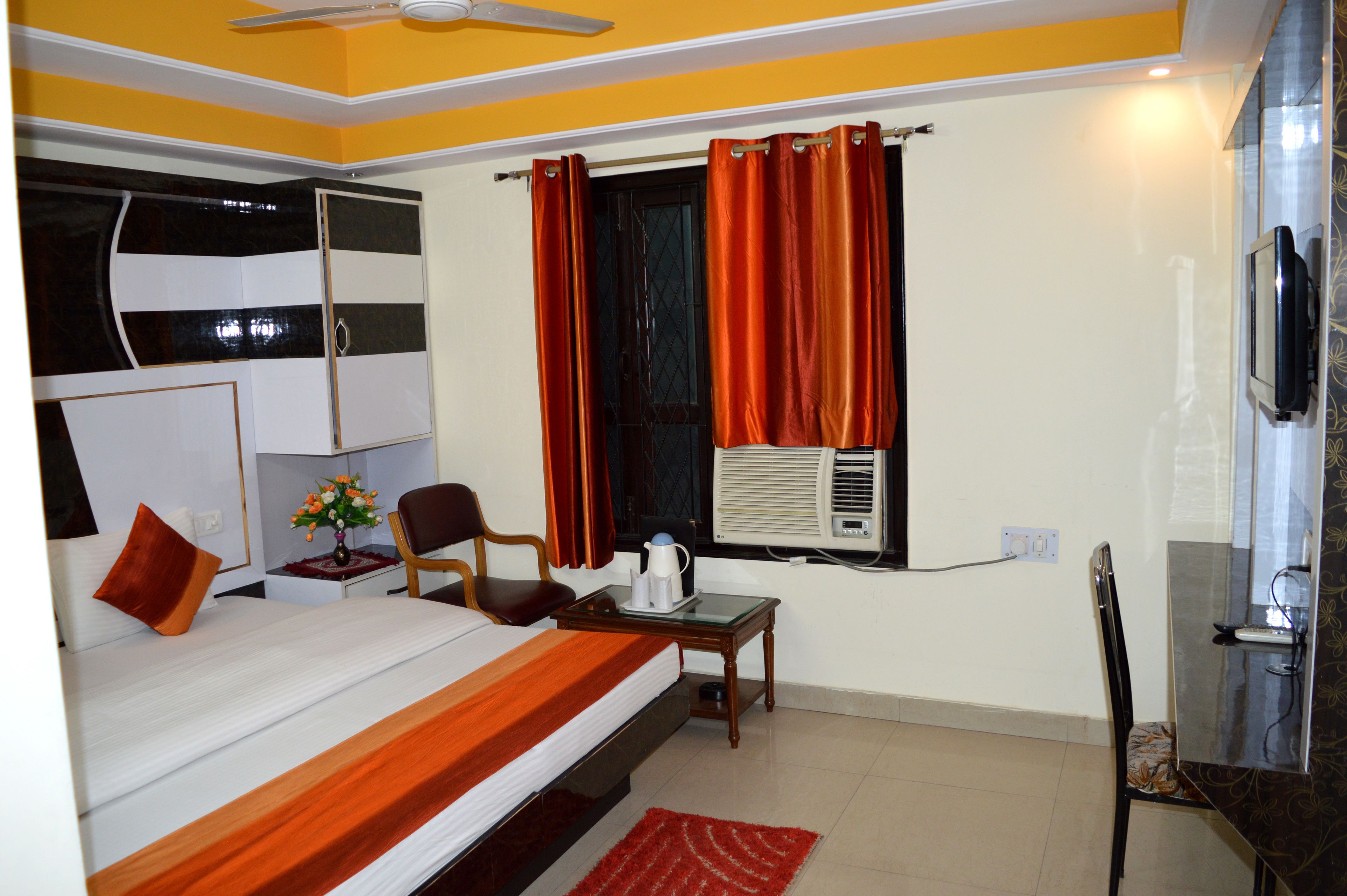 A hotel room with a bed, a desk, a chair, a TV, and an air conditioning unit.