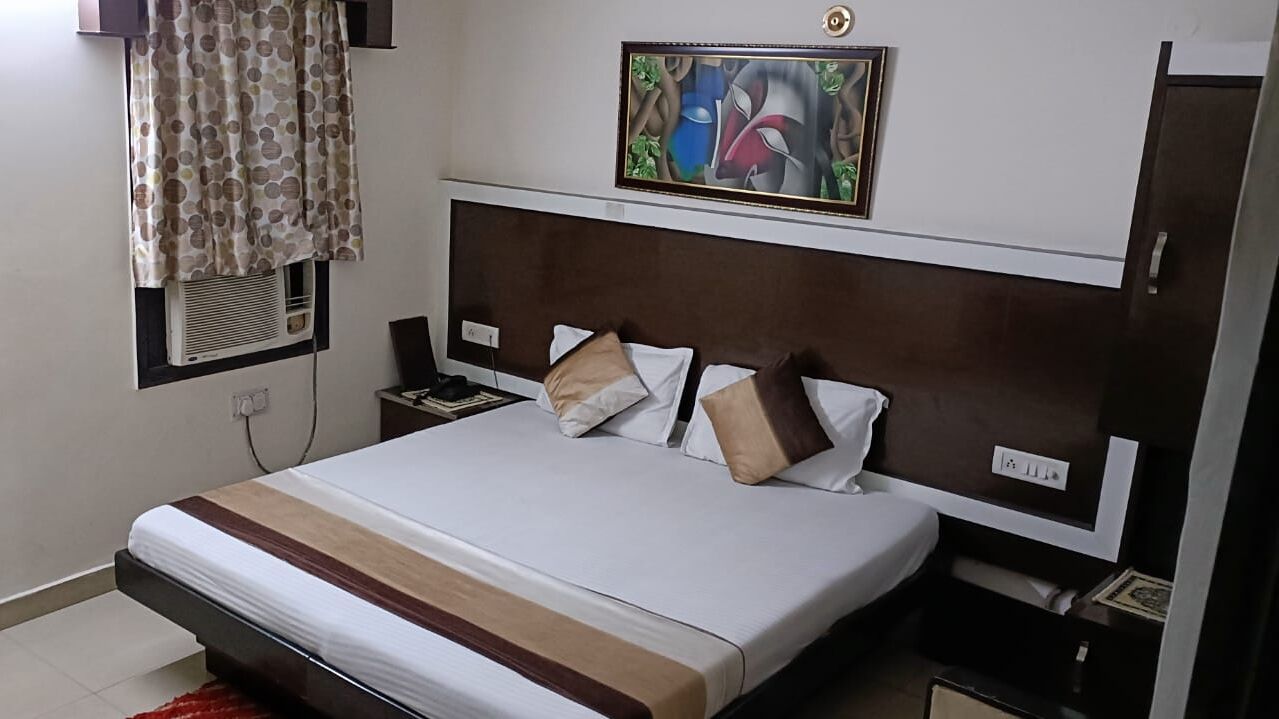 Een slaapkamer met een groot bed, een hoofdbord, een nachtkastje, een wandairconditioner, een schilderij en een raam met gordijnen.