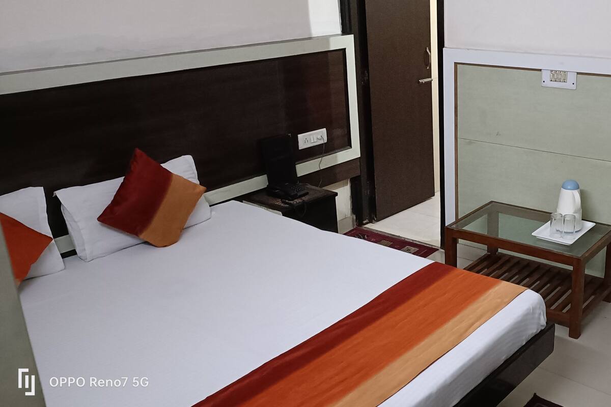 A hotel room with a bed, bedside table, chair, and an air conditioning unit.