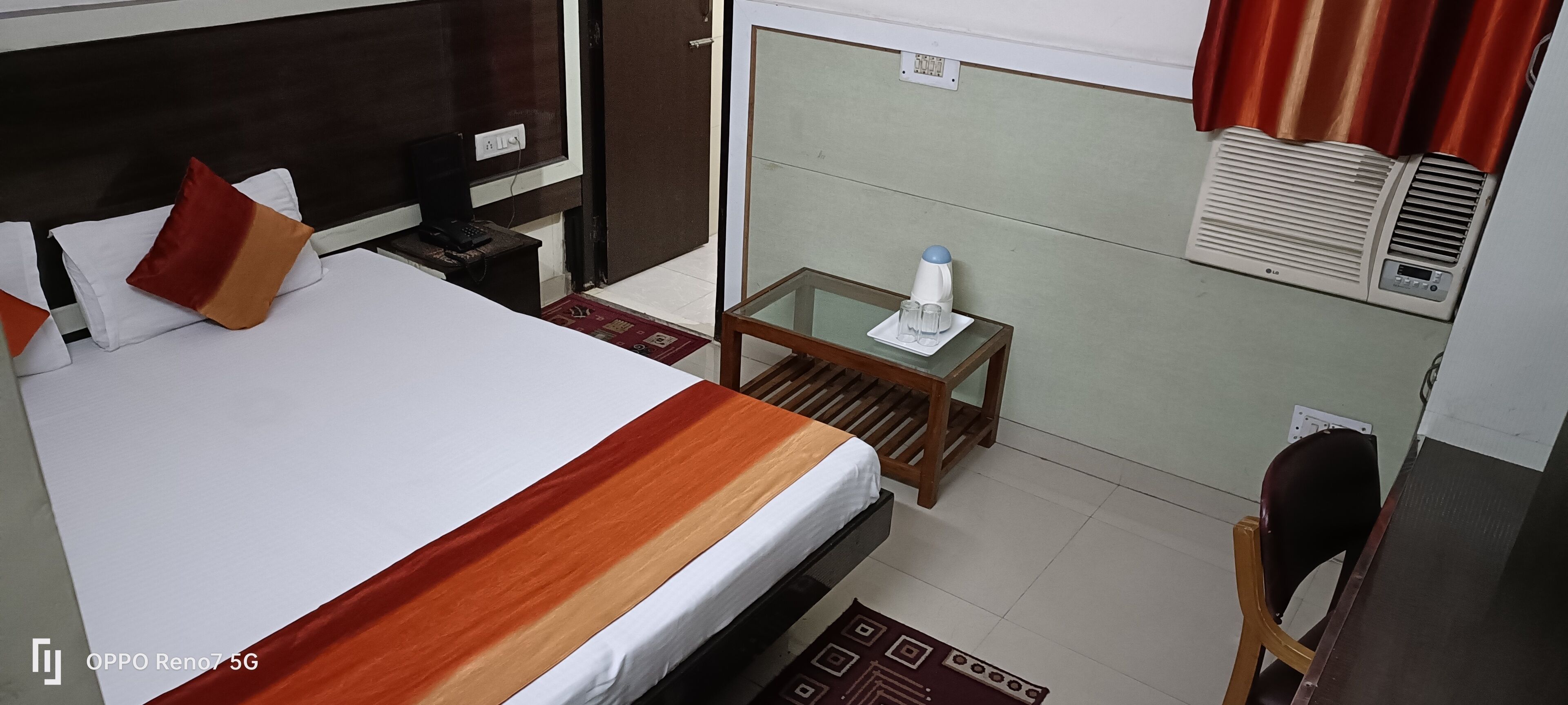 Een hotelkamer met een bed, nachtkastje, stoel en een kleine tafel met een waterfles en glazen.