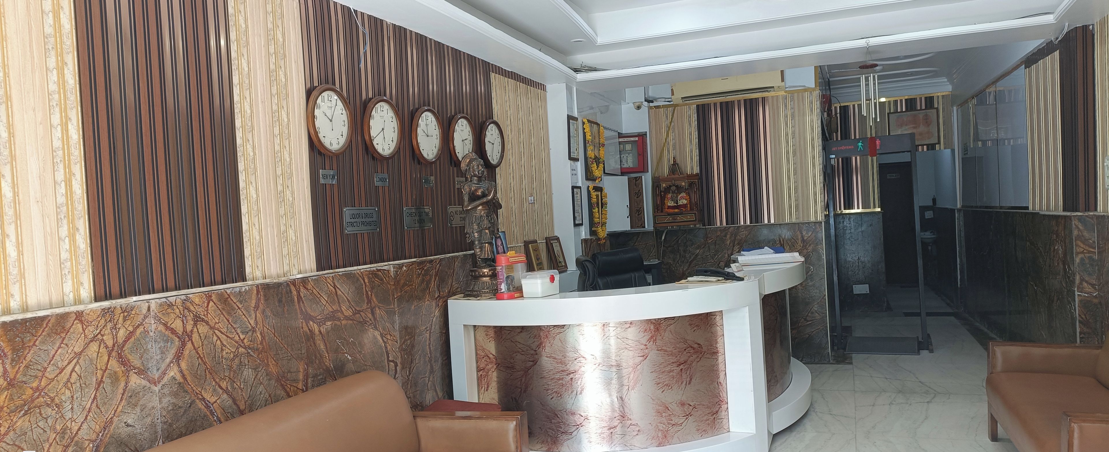 Zona de recepción con pared de mármol, mostrador de recepción y área de estar con sofás de cuero.