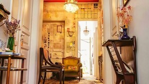A hallway with a chandelier, a wooden chair, and a table with a vase of flowers.