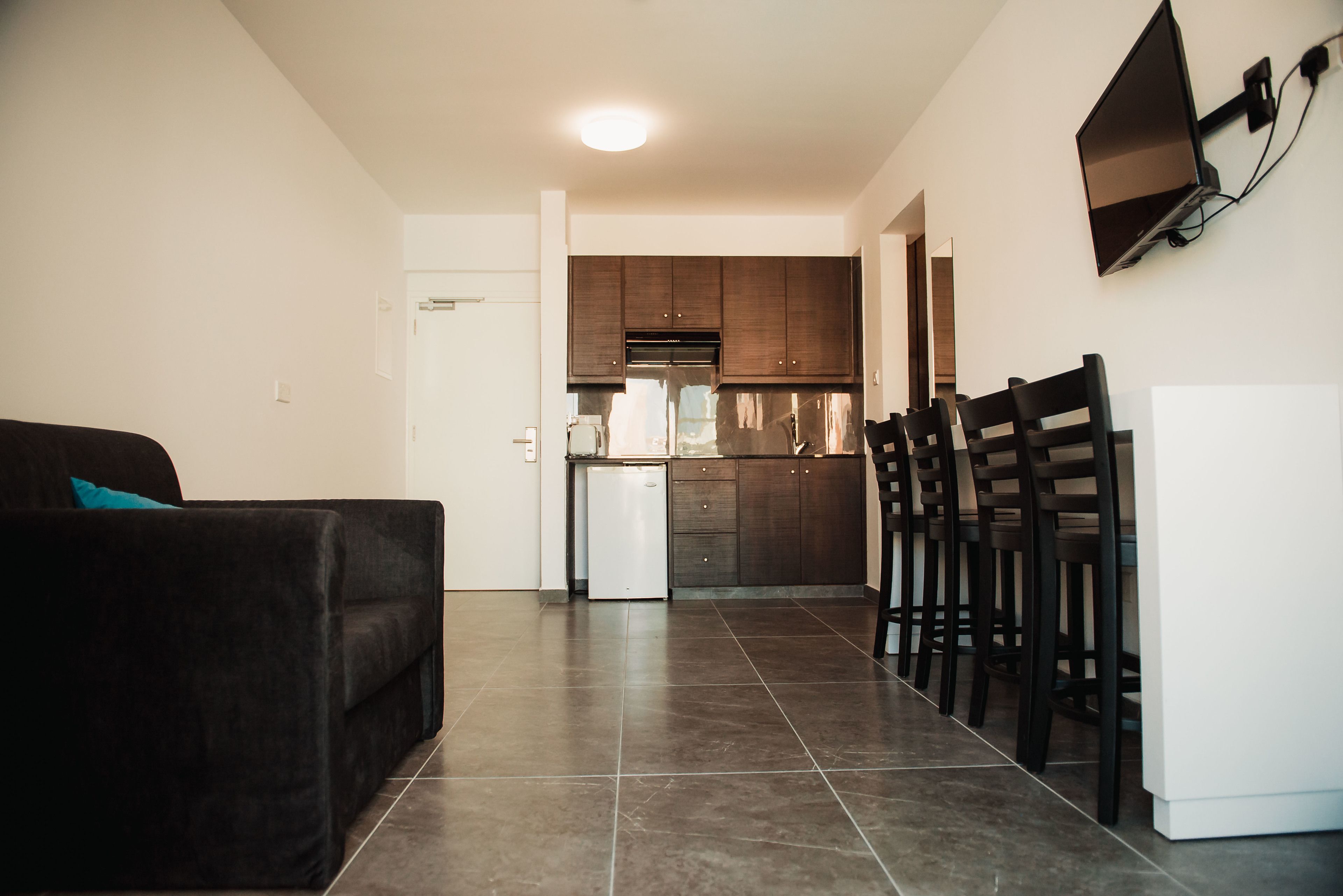 A modern living room with a dark sofa, a small white refrigerator, and a dining area with wooden chairs and a table.