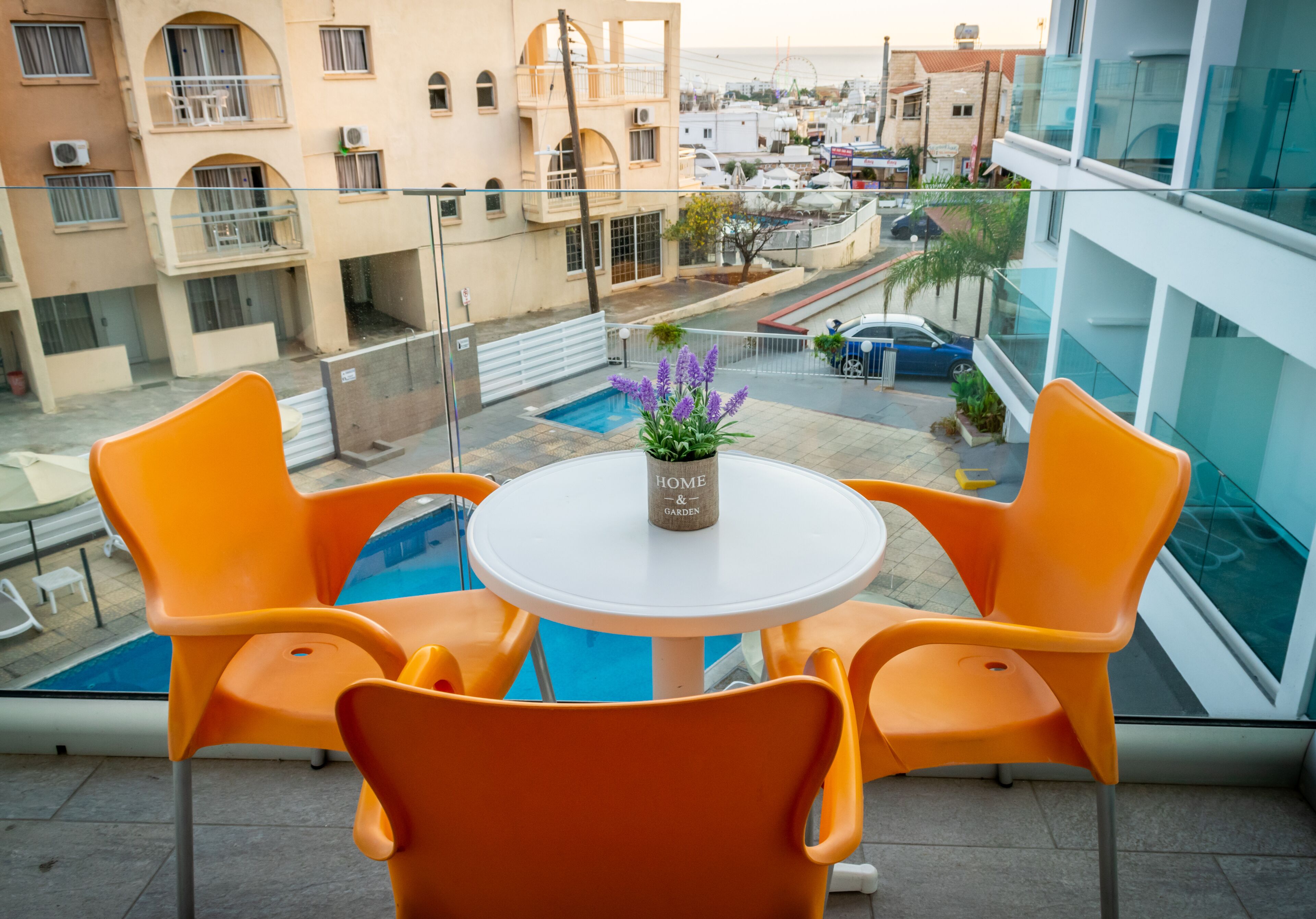 Ein Balkon mit orangefarbenen Stühlen und einem Tisch, der auf einen Pool und die Stadt blickt.