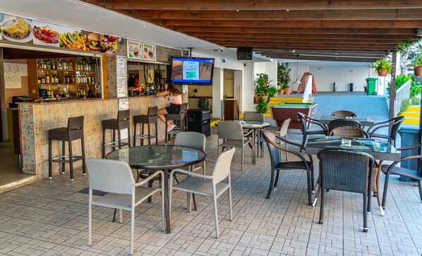 An outdoor seating area with wicker chairs and tables, a bar with a stone counter, and a pool table.