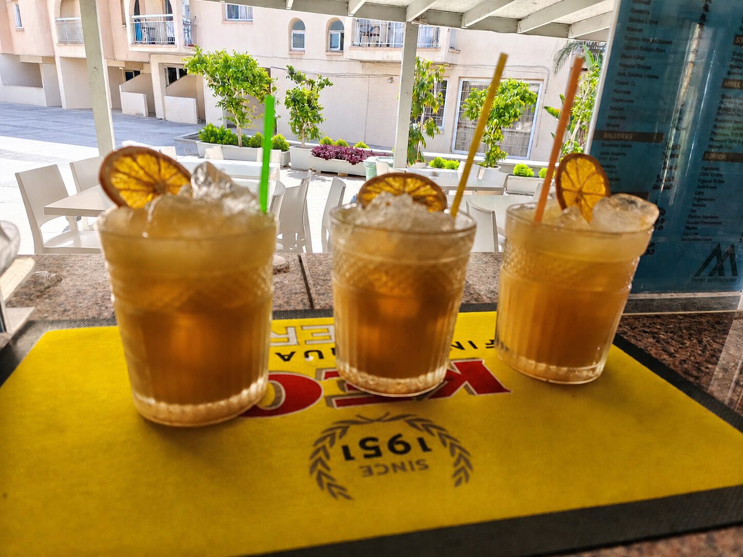 Three glasses of iced tea with orange slices on a yellow coaster with 'VIC' and '1975' text.