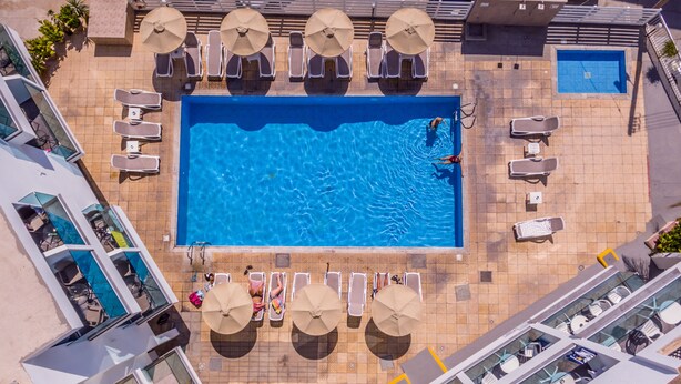 Vista aerea di una zona piscina con numerosi lettini, ombrelloni e una piccola vasca.