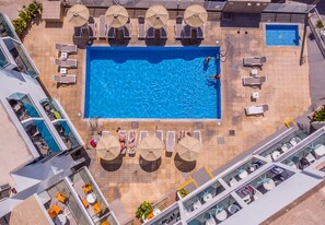 An aerial view of a hotel pool area with multiple sun loungers, umbrellas, and a small pool.