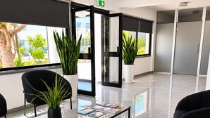 Un'area d'attesa moderna con un tavolino in vetro, sedie nere, piante in vaso e vista sull'esterno.