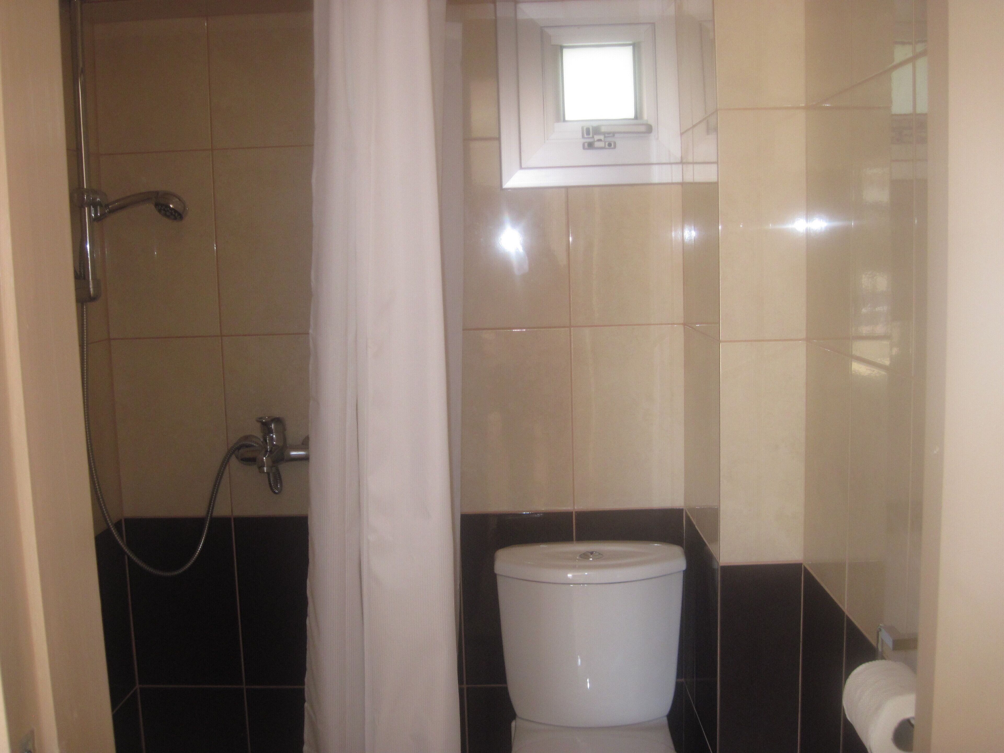 Un baño con ducha, inodoro y un pequeño ventanal sobre el lavamanos.