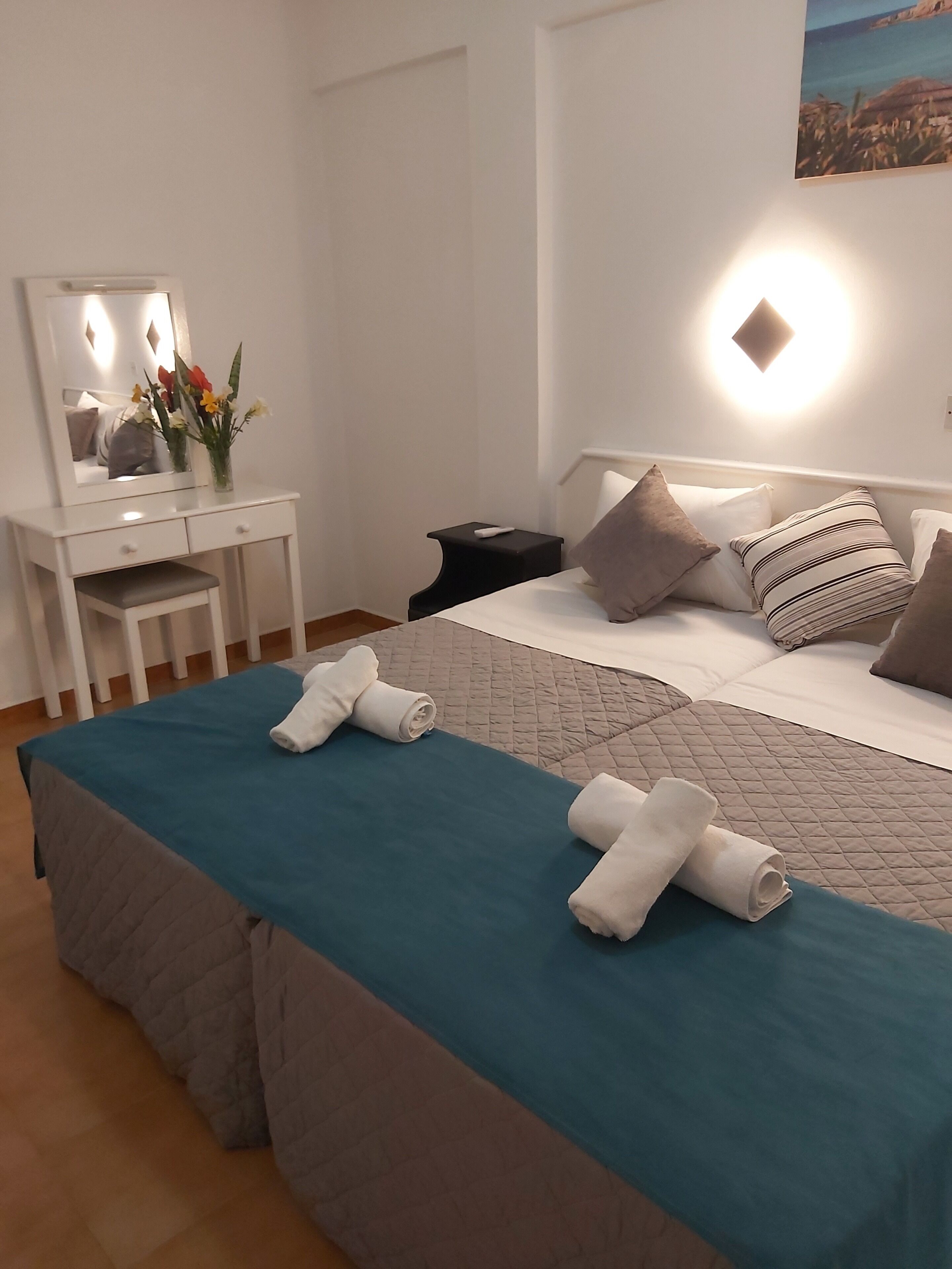 A hotel room with a bed, a bedside table, a dresser, and a mirror.