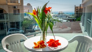Un balcone con tavolo e sedie, un vaso con fiori e vista sul mare e sugli edifici.
