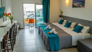 Una camera d'albergo con un letto, una scrivania con sedie, un balcone con vista sulla città e un quadro appeso al muro.