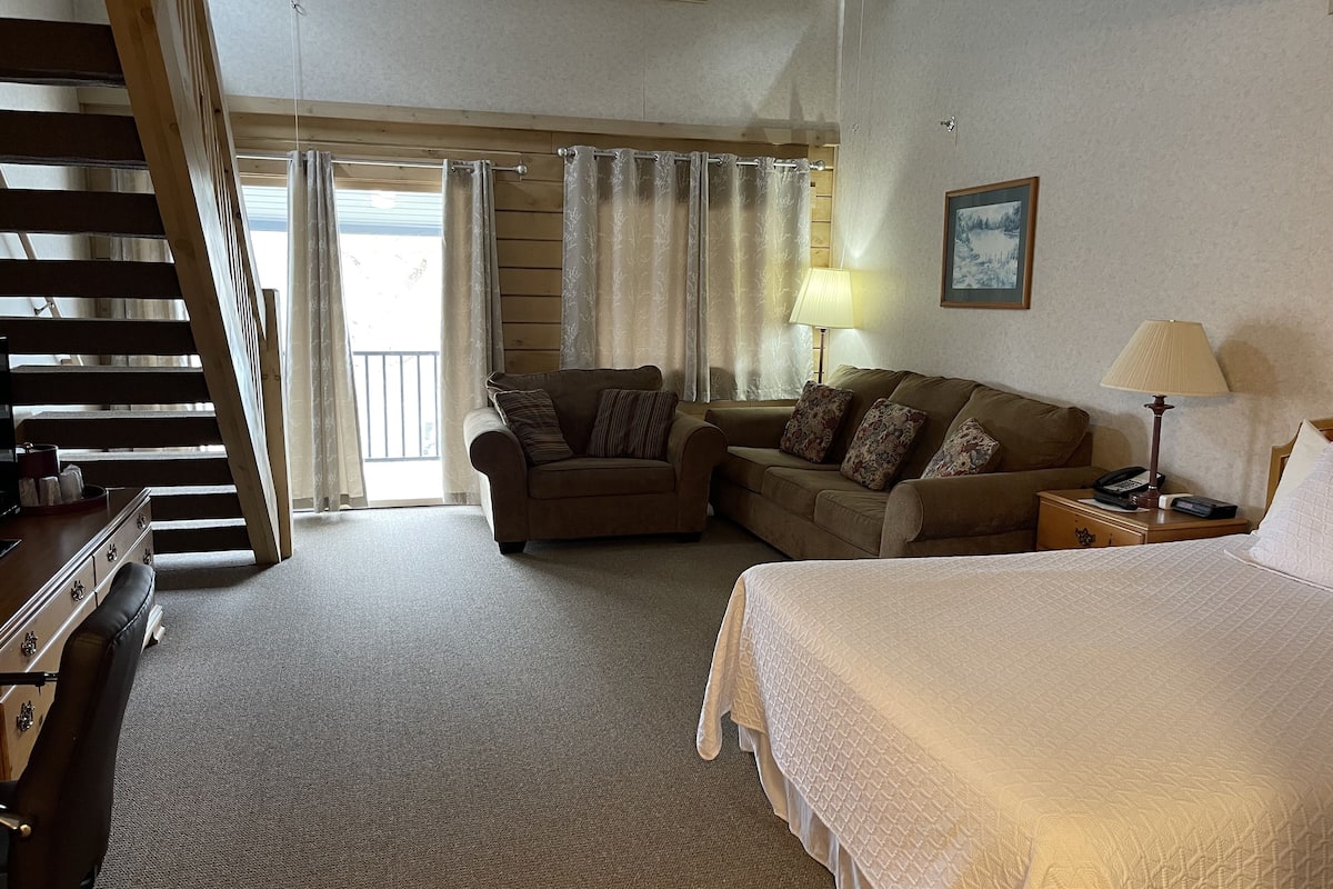 A hotel room with a bed, a sofa, a chair, a desk, and a staircase.