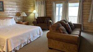 A cozy room with a large bed, a brown sofa, and a chair. There are two lamps on a nightstand. - Paddle Wheel Inn (Oregon)