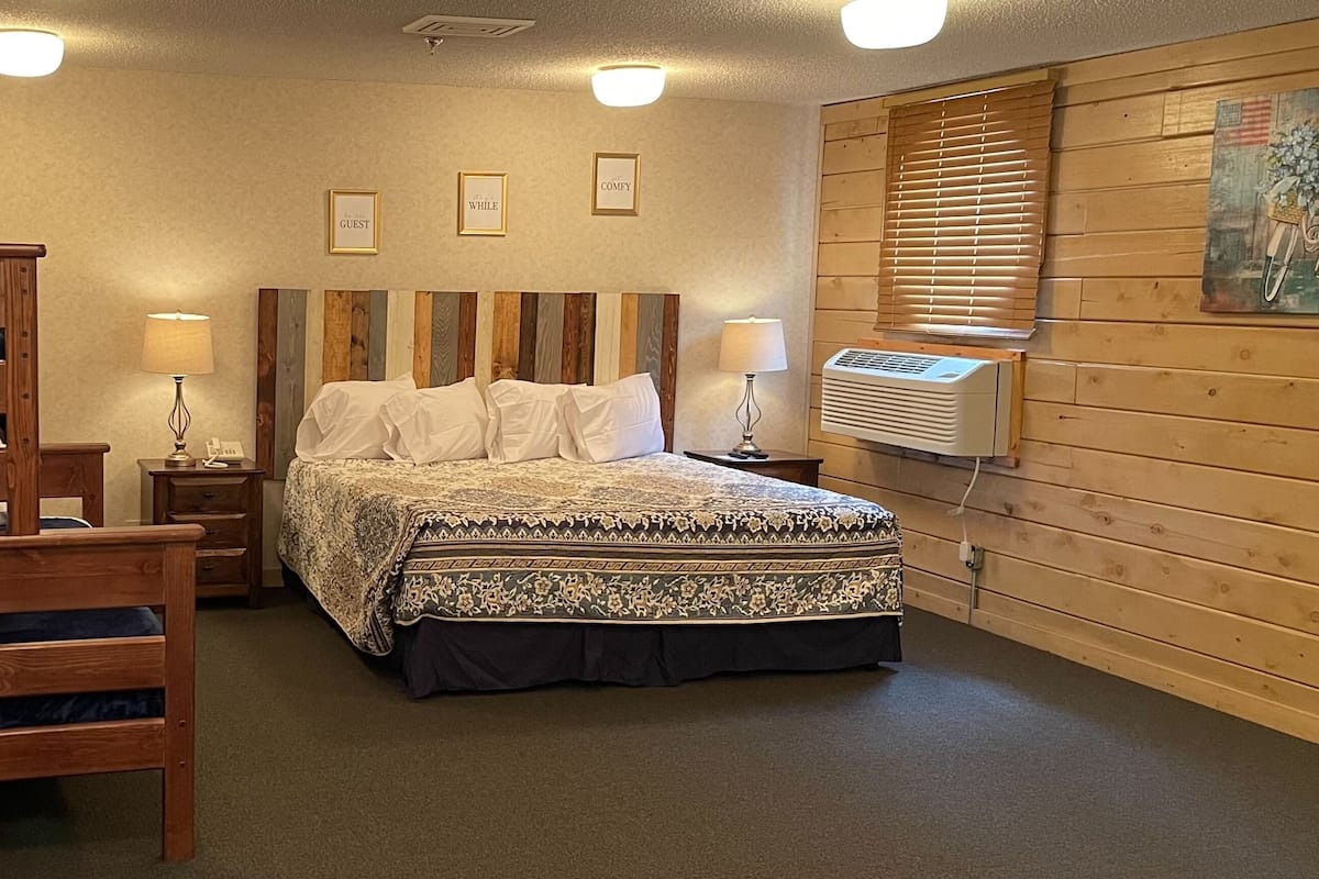 A bedroom with a wooden bed, a wooden chair, a bedside table with a lamp, and a wall-mounted air conditioner.