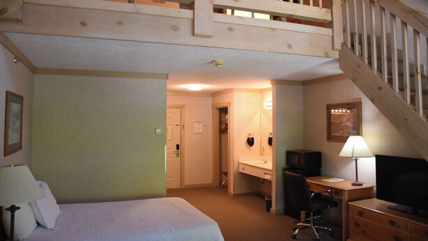 A hotel room with a bed, desk, chair, television, and a staircase. - Paddle Wheel Inn (Oregon)