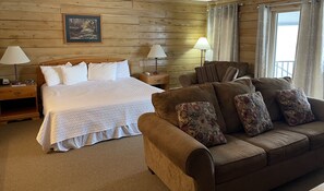 A wooden-paneled room with a bed, two bedside lamps, a patterned sofa, and a framed picture on the wall.