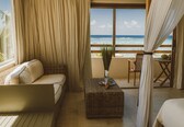 A balcony with a view of the ocean, wicker furniture, and a small table with a plant.