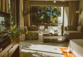 A hotel room with a large window, a sofa, a coffee table, and a TV.