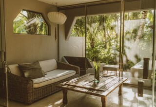 A modern living room with a wicker sofa, a glass coffee table, and a view of lush greenery outside.