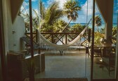 A room with a hammock, wicker furniture, and a view of the ocean and palm trees.