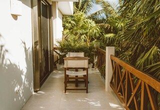 A corridor with a wooden table and chairs, surrounded by lush greenery and a wooden railing.