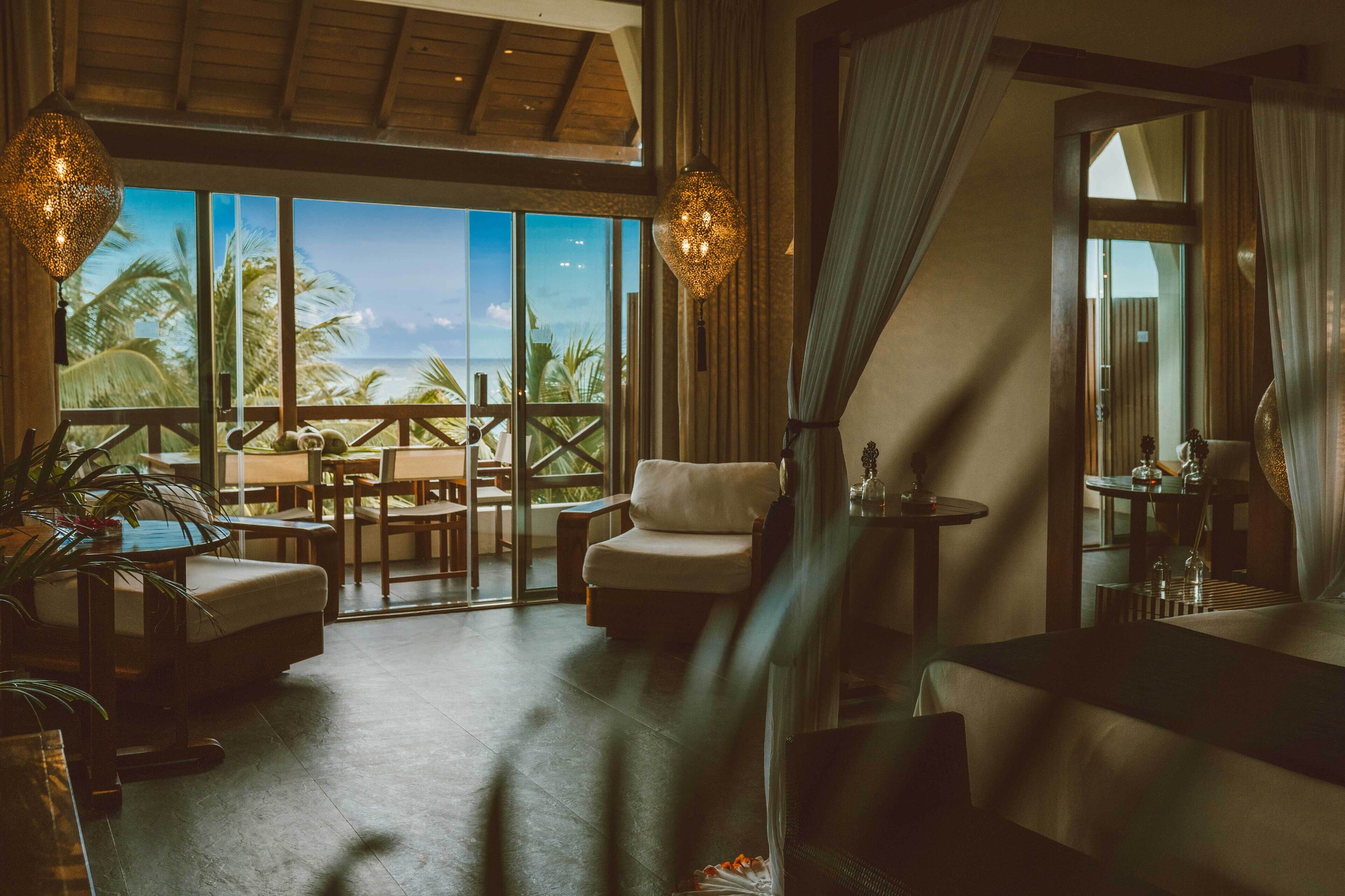 A spacious room with a large balcony overlooking the ocean, furnished with a sofa, chairs, and a dining table.
