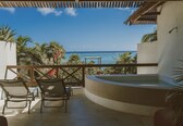 A balcony with a view of the ocean, a hot tub, and lounge chairs.