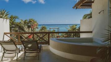 Un balcón con vista al océano, un jacuzzi y sillones de descanso.
